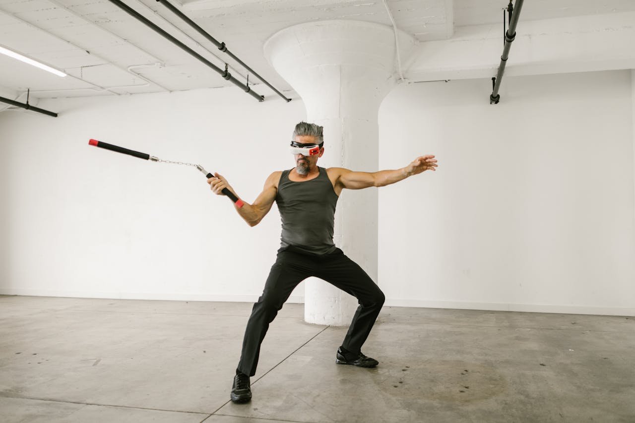 Adult man skillfully using nunchaku with VR headset in an indoor setting, showcasing future tech integration.